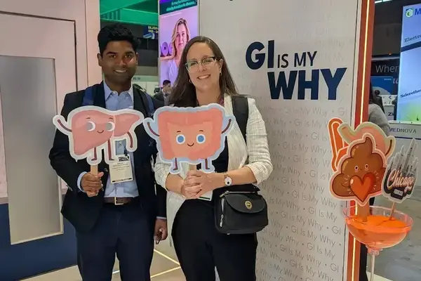 Smiling man in suit holds a pink liver cutout. Smiling woman in glasses holds pink intestine cutout at alimentiv GI booth.